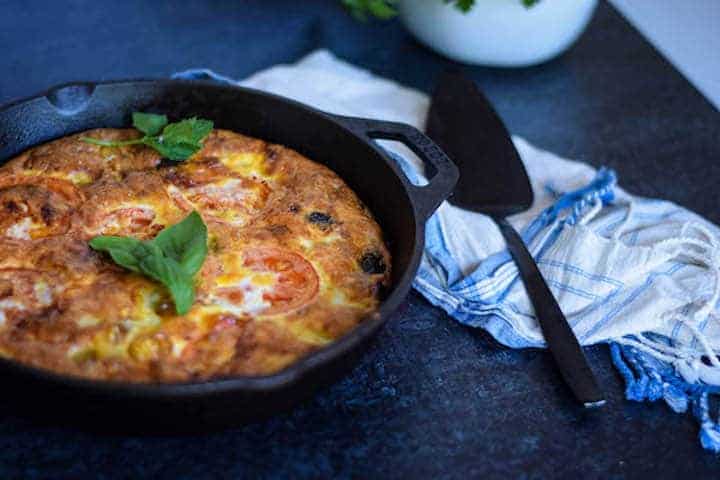 finished frittata in cast iron skillet with a blue tea towel