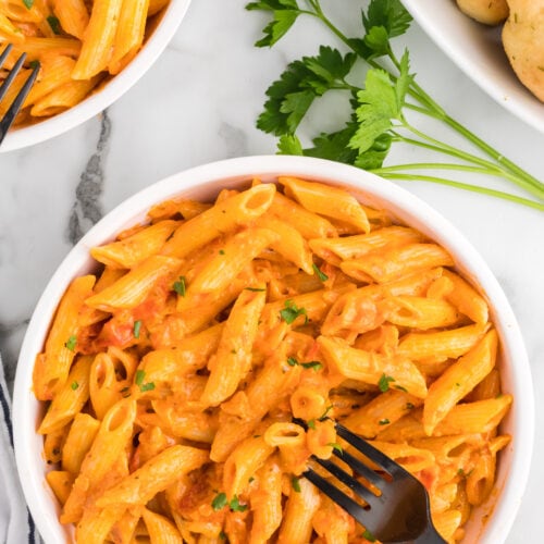 white bowl of creamy pomodoro sauce with penne pasta and a black fork.
