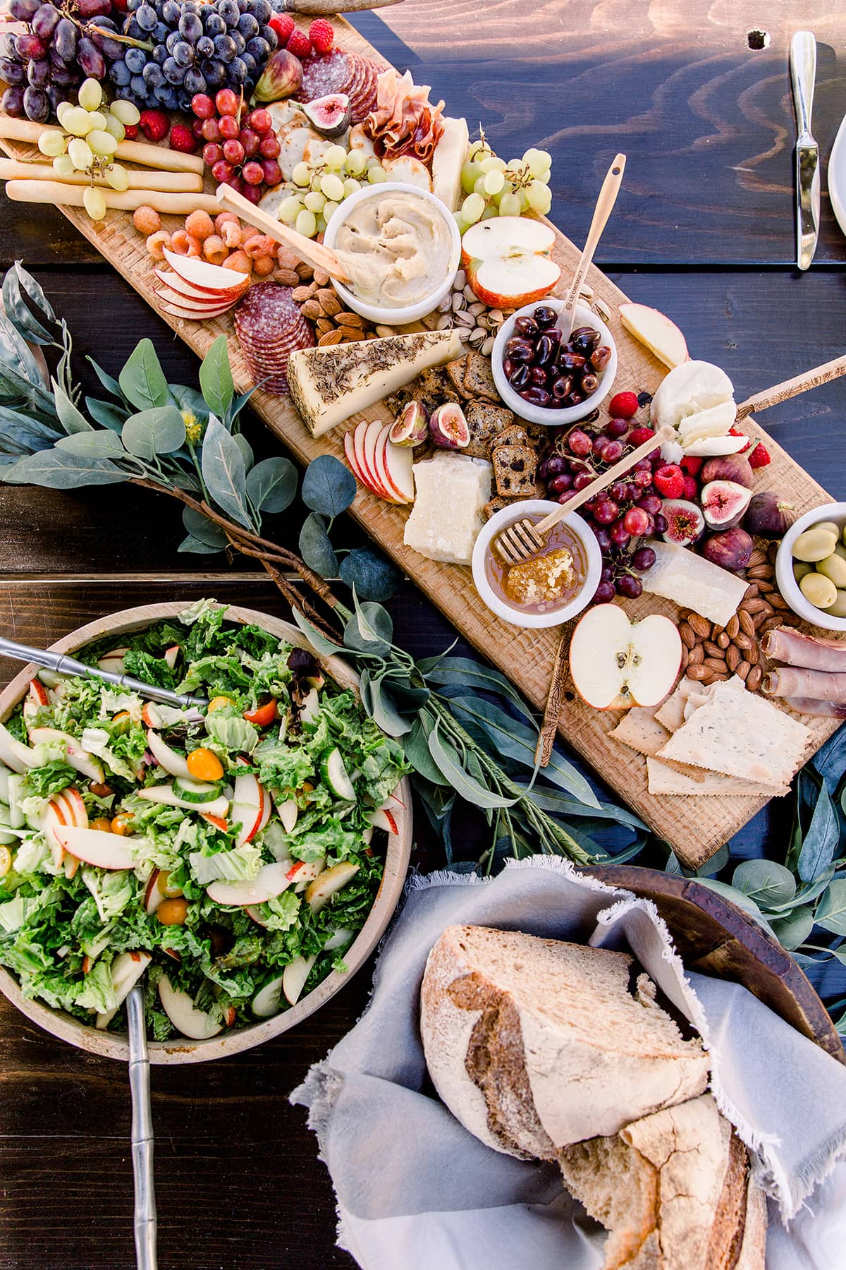 family table set with fruits, nuts, cheeses, a large fresh veggie salad.