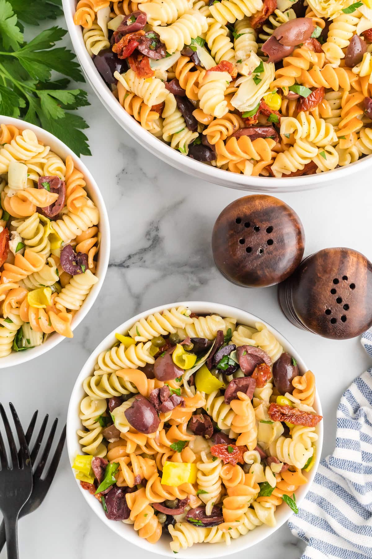 large serving bowl and two white bowls with the finished Mediterranean pasta salad.