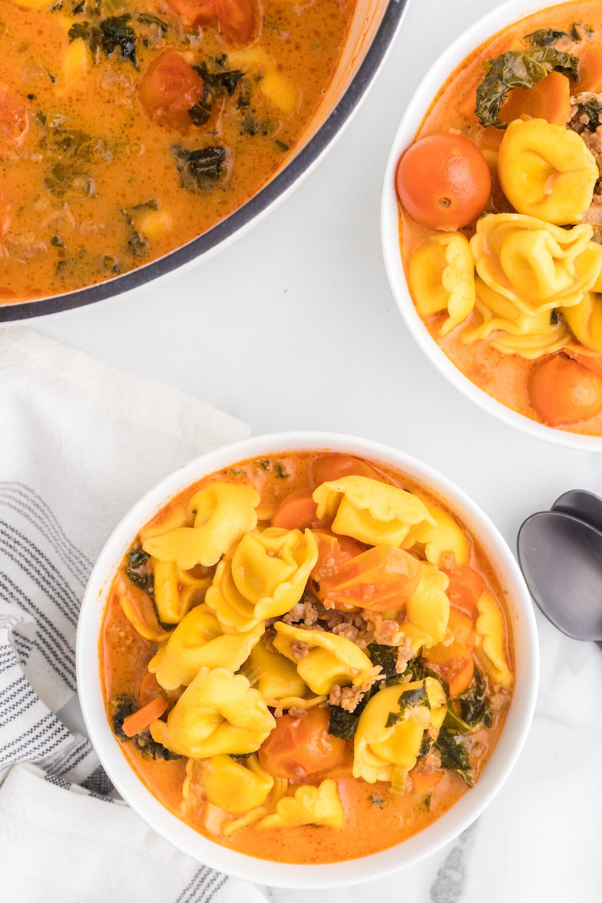 two white soup bowls filled with creamy sausage tortellini soup and dutch oven to the back.