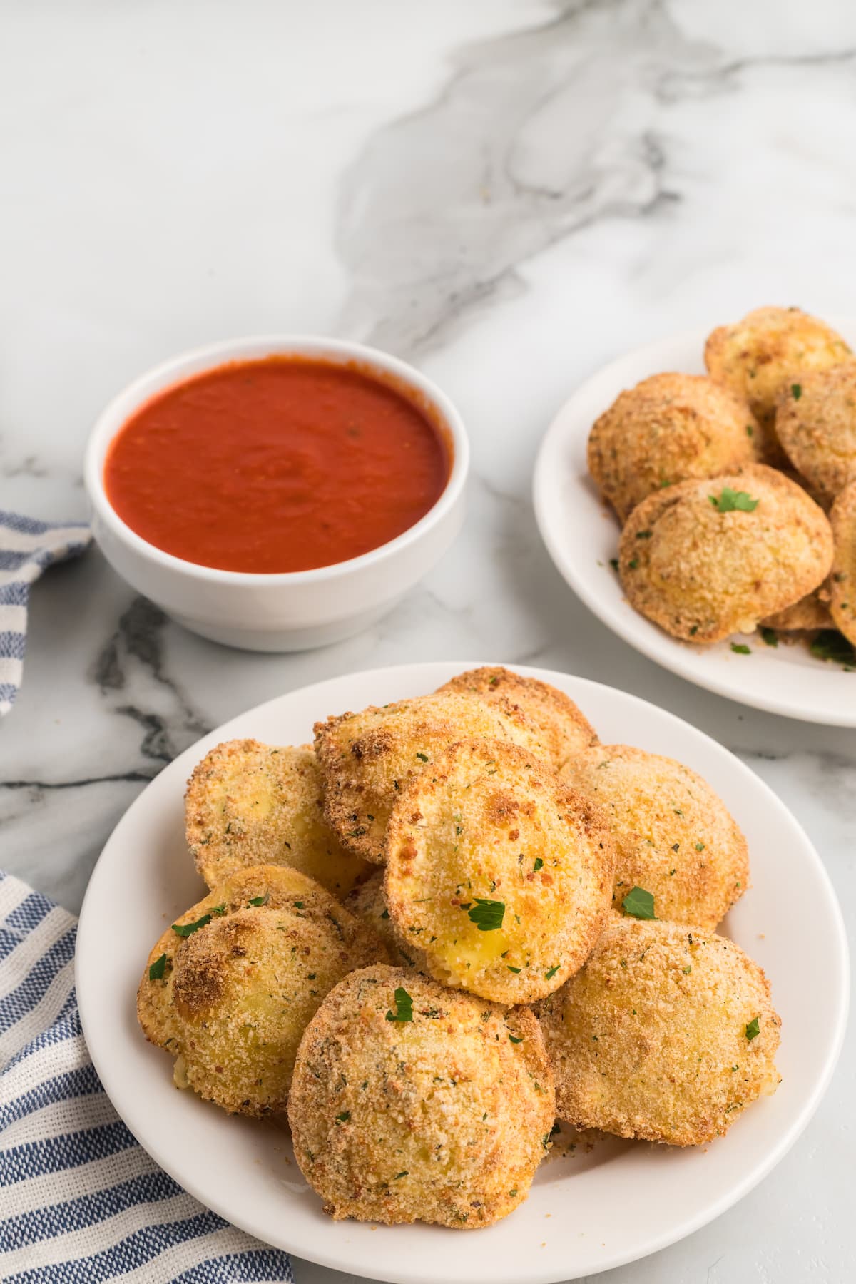 air fryer crispy ravioli on a white plate with a small white bowl of marinara sauce behind.
