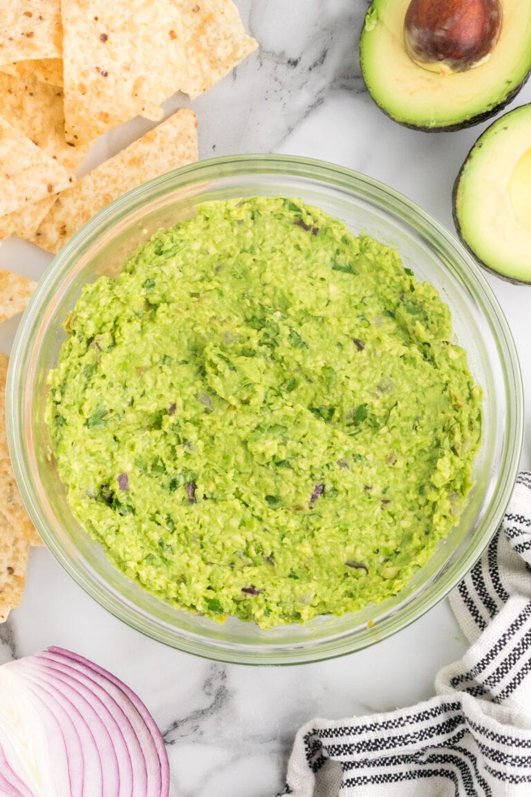 glass bowl of homemade guacamole without tomatoes and tortilla chips surrounding.