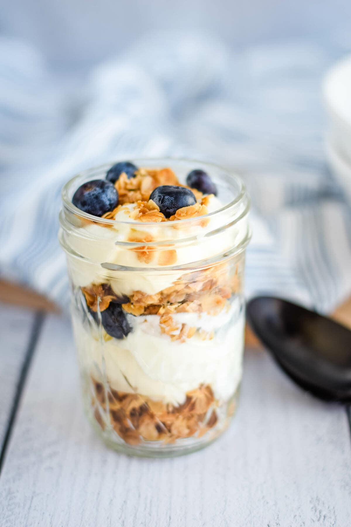 healthy homemade granola layered in a pint sized mason jar with fresh blueberries and yogurt.
