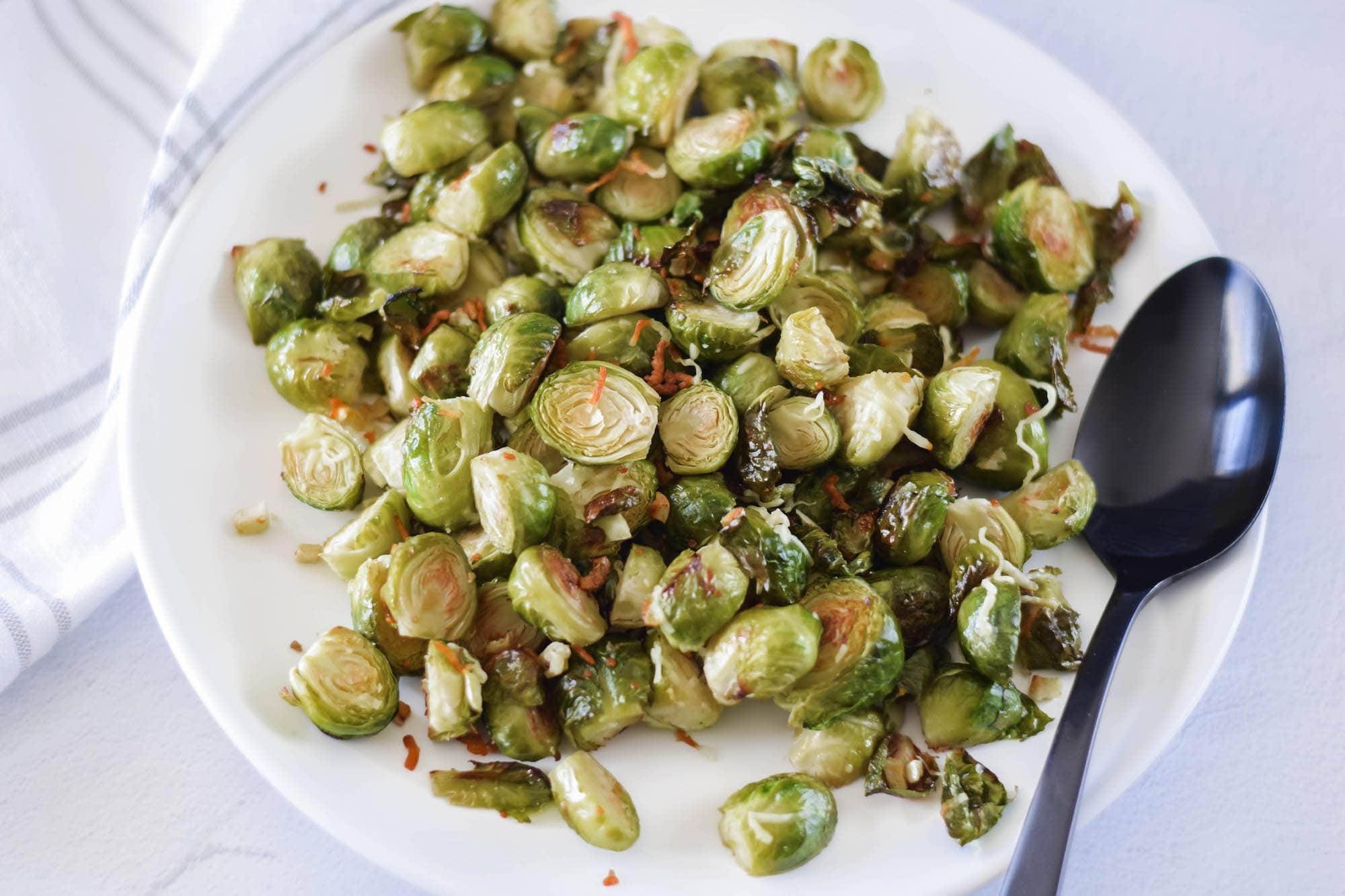 white platter of Roasted Brussels sprouts with a black spoon resting to the side.