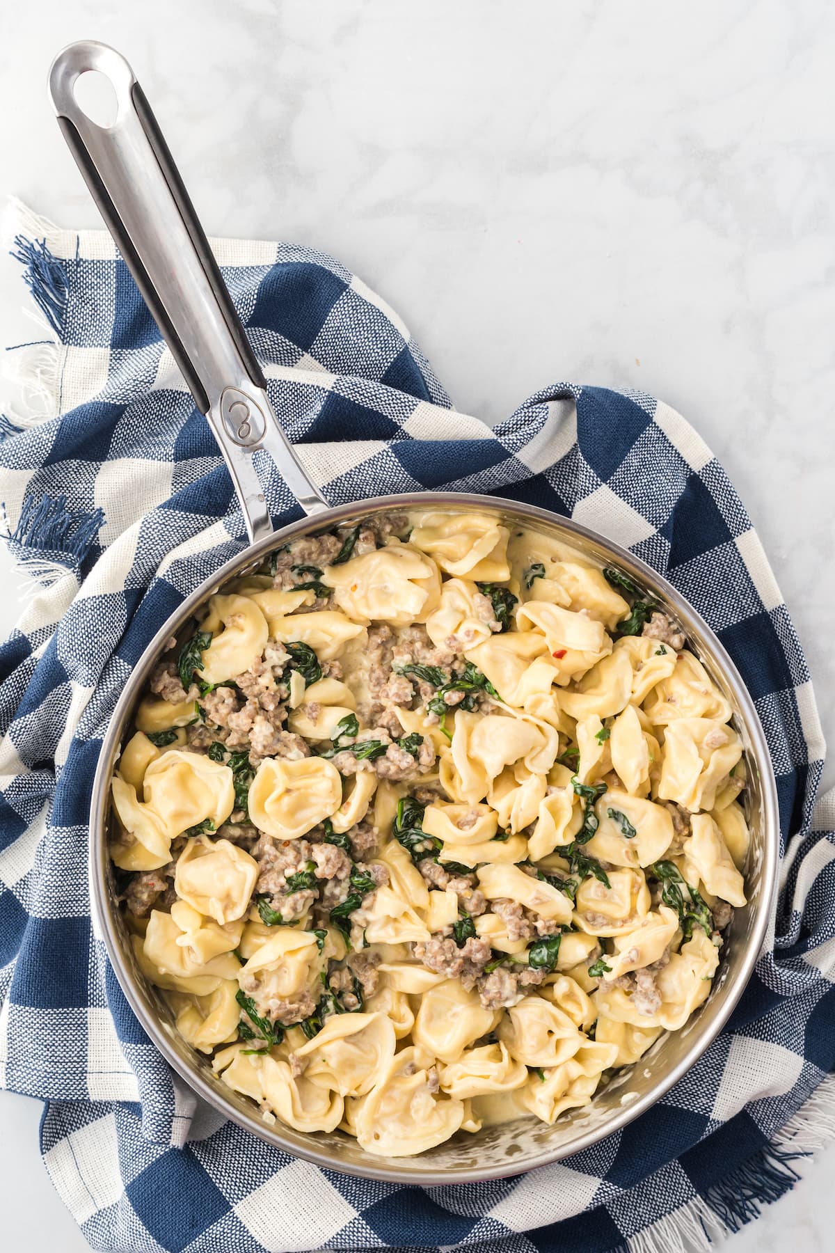 large skillet with creamy tortellini and italian sausage.