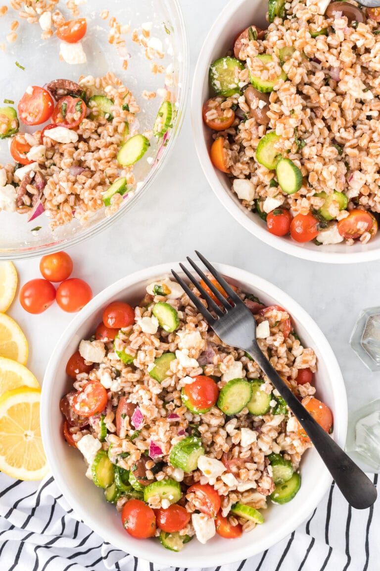 two white bowls of farro salad with mediterranean seasonings and fresh veggies.