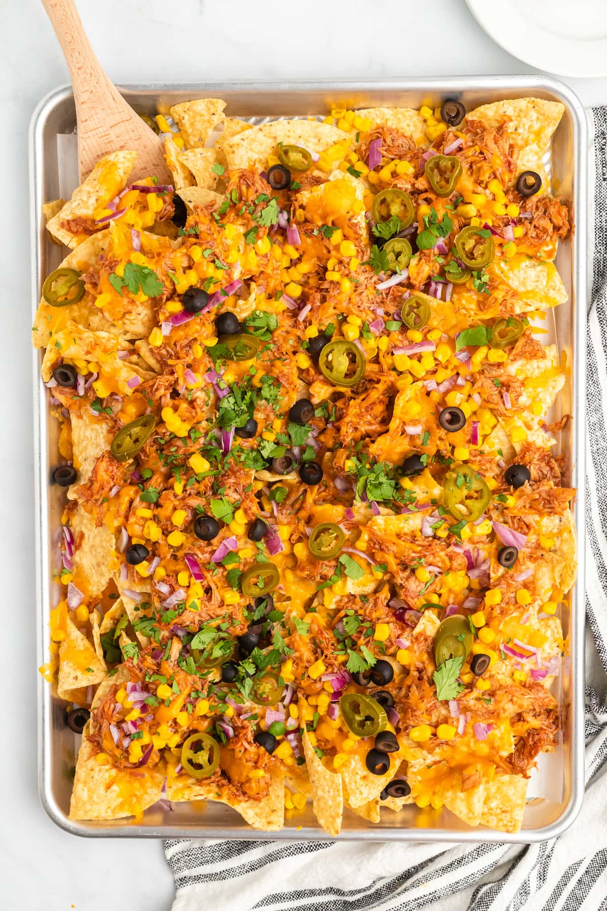 bbq nachos on a sheet pan with a black and white striped tea towel behind it. 
