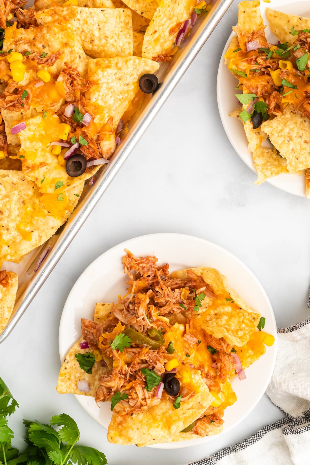 bbq chicken nachos on a sheet pan and white plates.