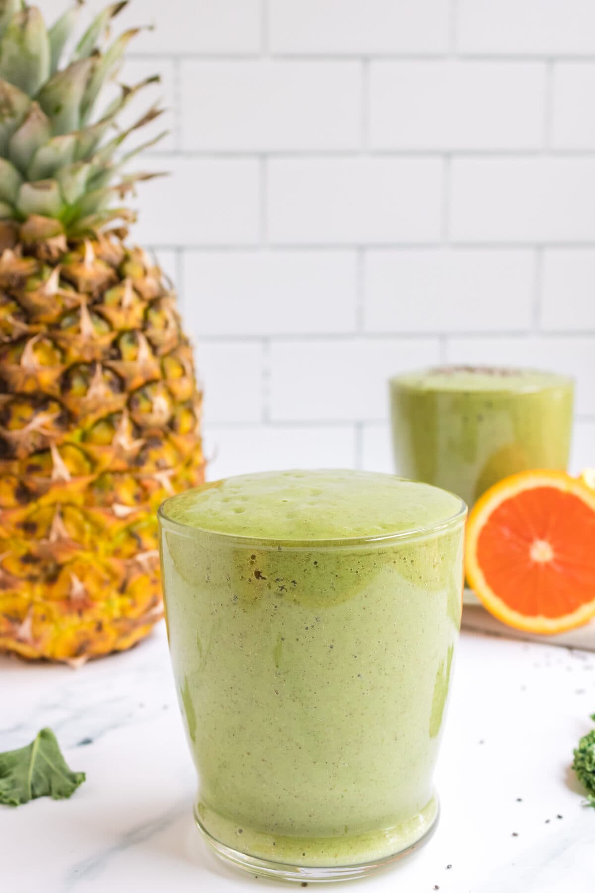 tropical green smoothie in a glass with pineapple in the background.