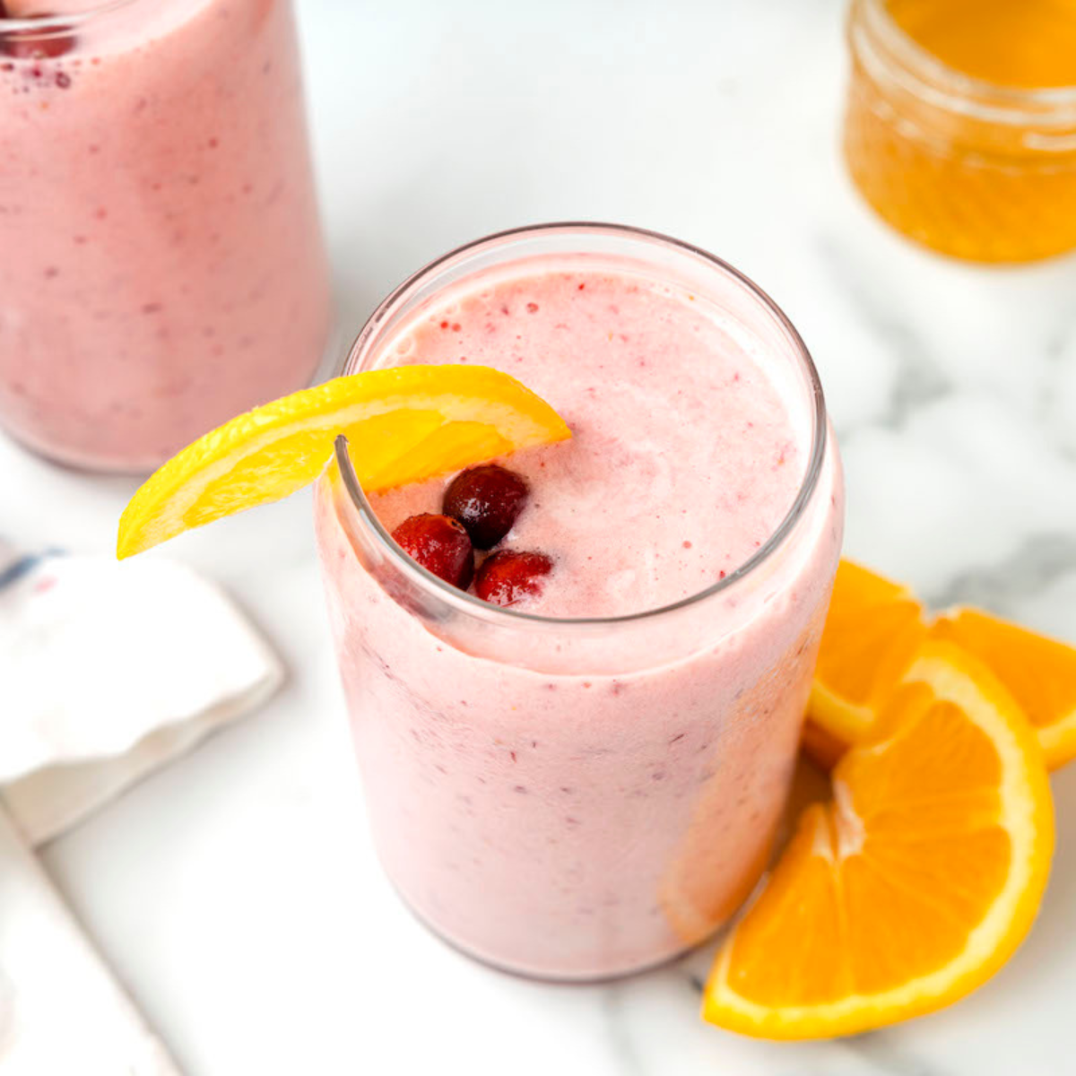 two glasses of cranberry smoothie with cranberry and orange garnishes.