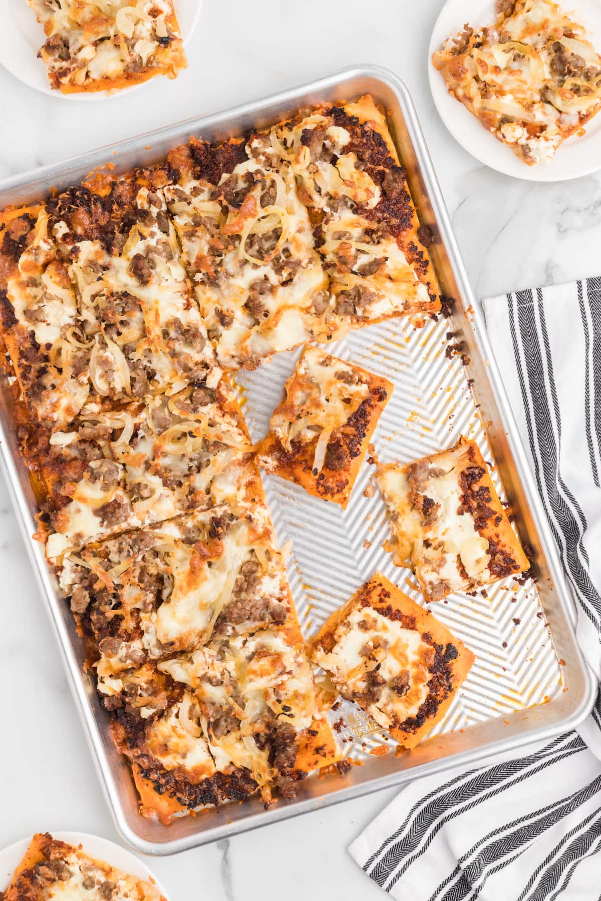 sheet pan with italian sausage pizza cut into square slices.