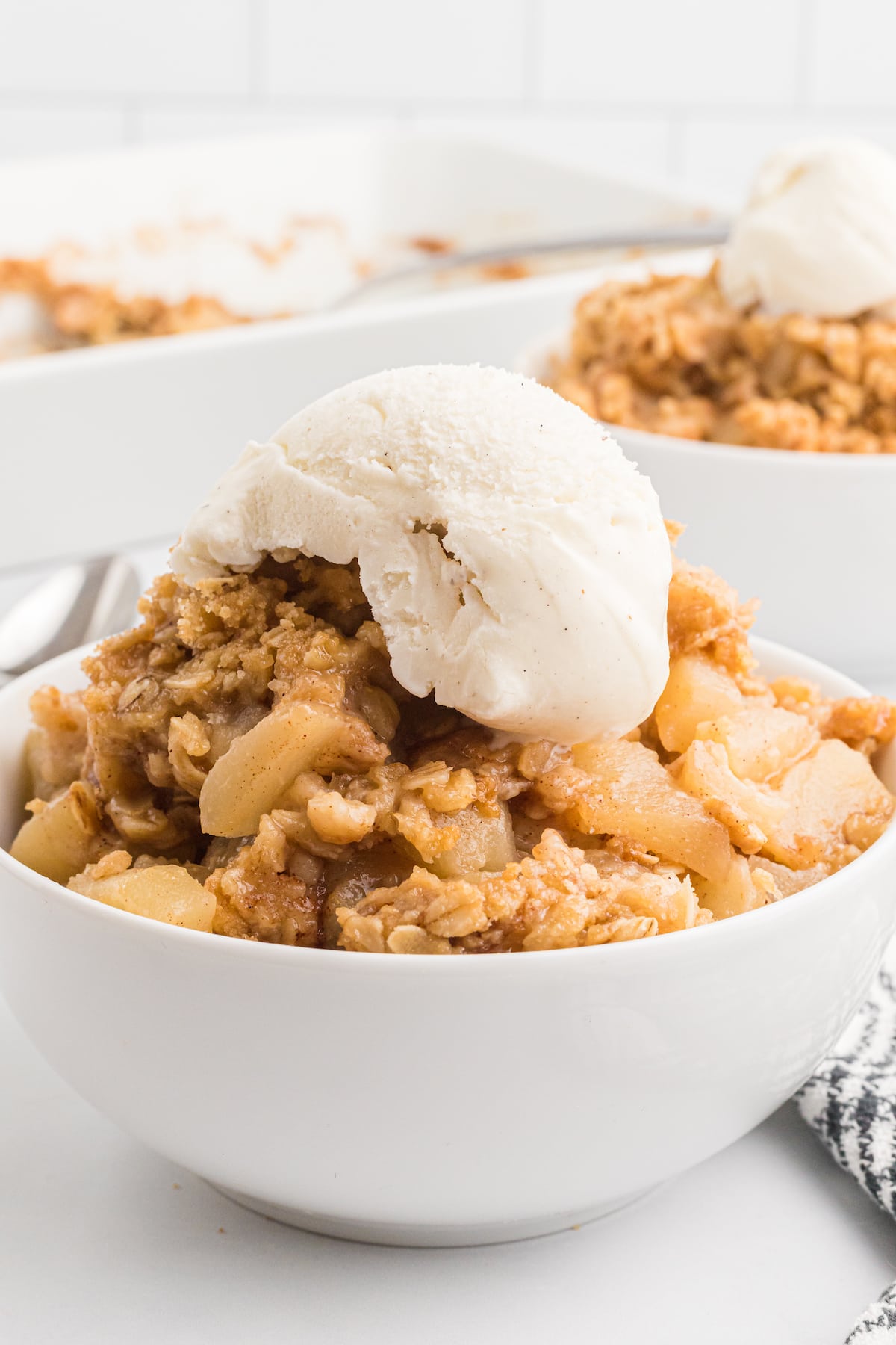 white dessert bowls filled with pear crisp and scoops of vanilla ice cream on top.