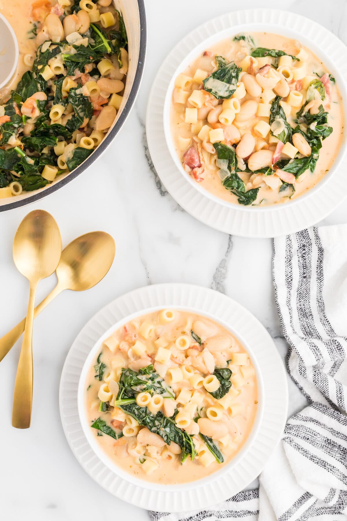 dutch oven and two white bowls of creamy pasta fagioli soup.