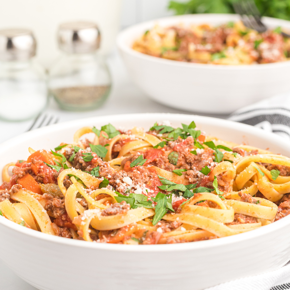 two white bowls of pasta with fresh herbs on top. 