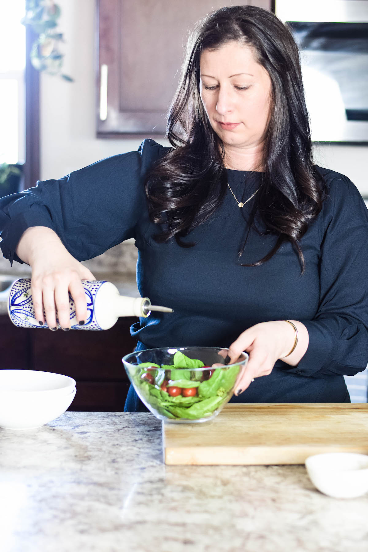 Mary in the kitchen pouring olive oil over a fresh salad.