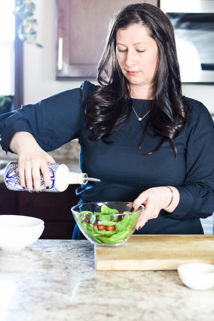 Mary pouring olive oil over a fresh salad. 