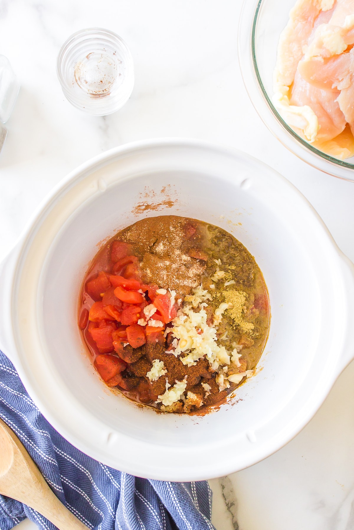 white slow cooker with tomatoes and seasonings at bottom. 