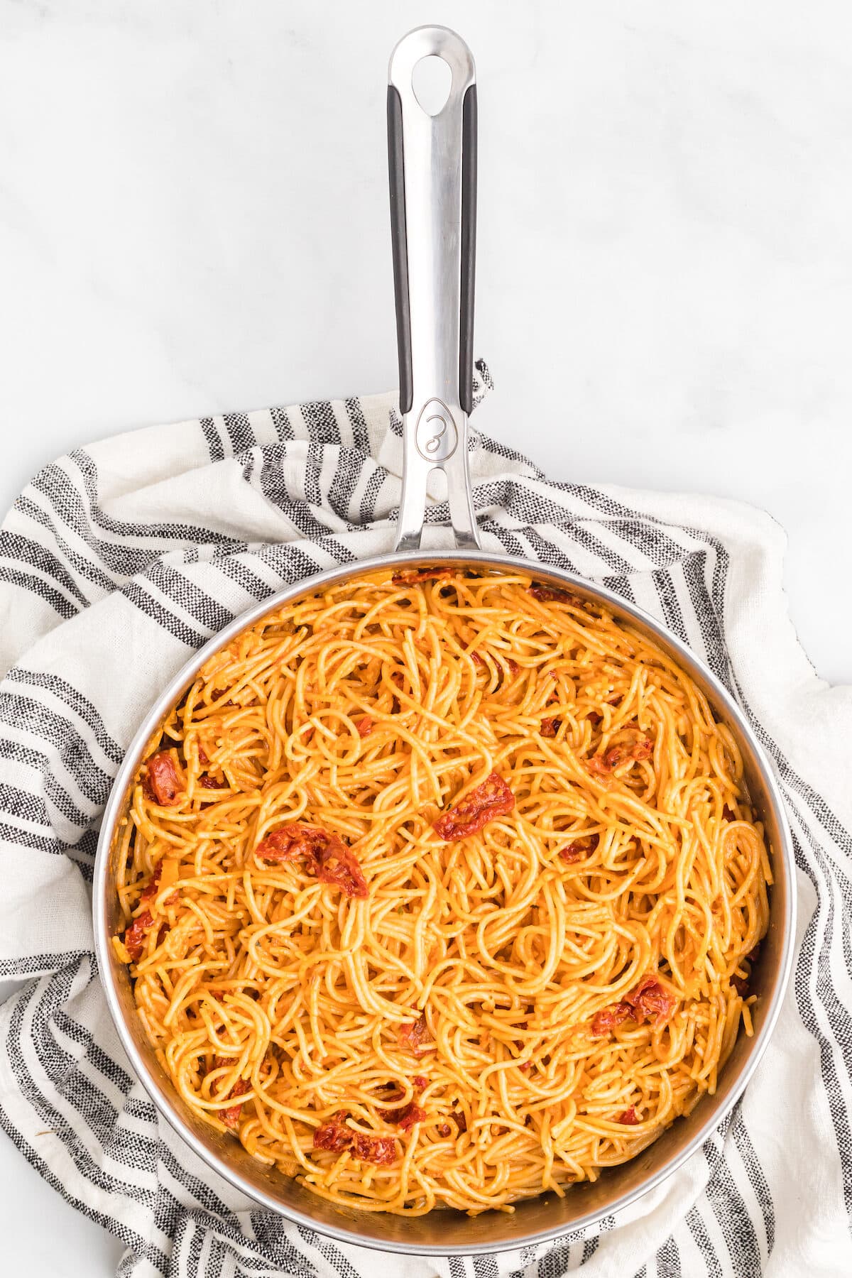 finished sun dried tomato cream sauce combined with spaghetti noodles in a skillet. 