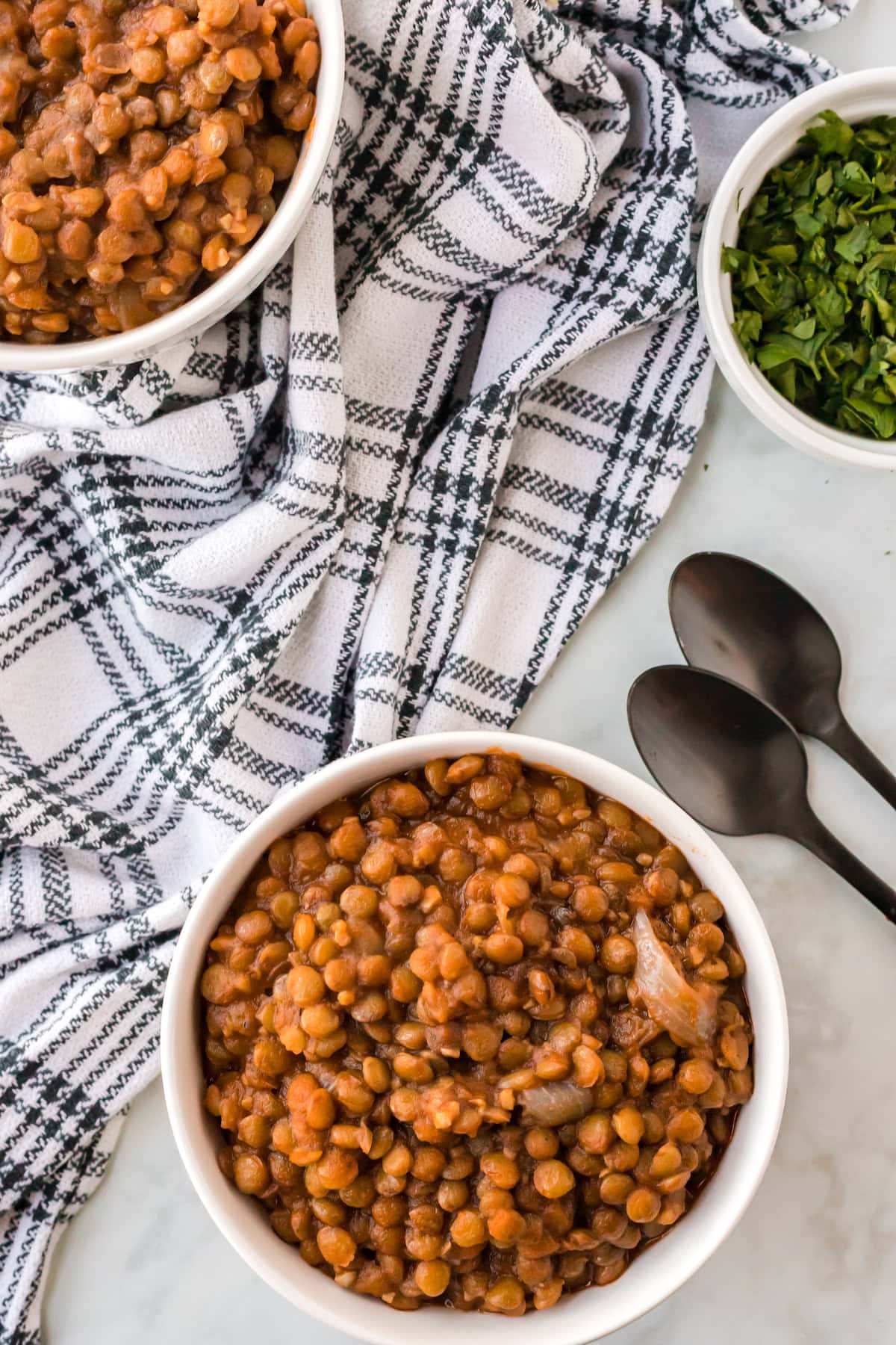 two white soup bowls with finished Mediterranean lentil soup with two black spoons resting to the side.