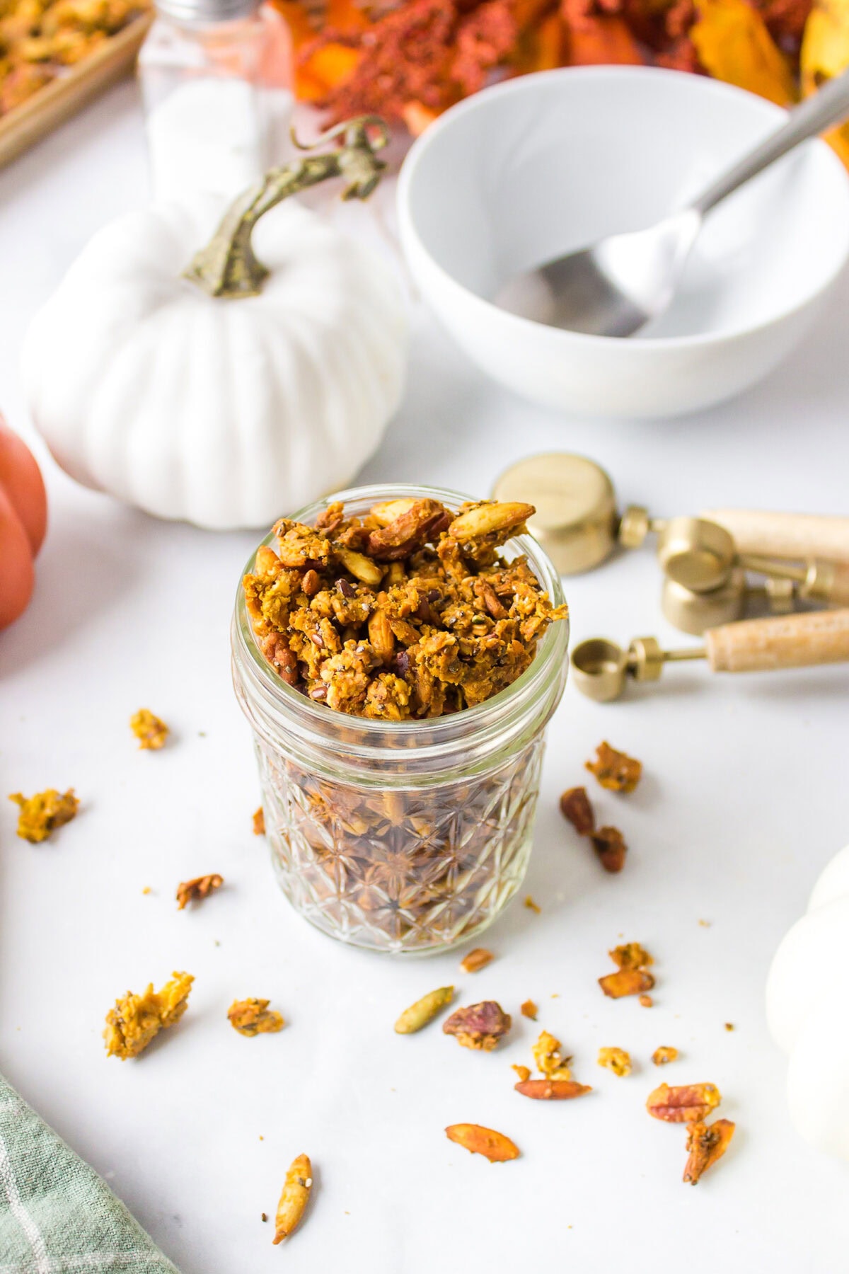 pumpkin maple granola recipe finished in a small mason jar with pumpkins in the background.