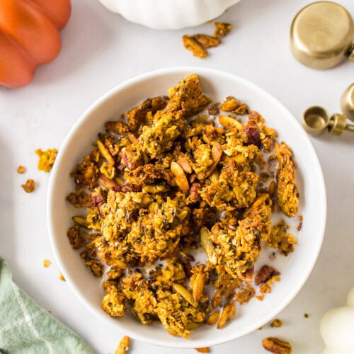 white bowl filled with finished maple pumpkin granola recipe and milk over top.