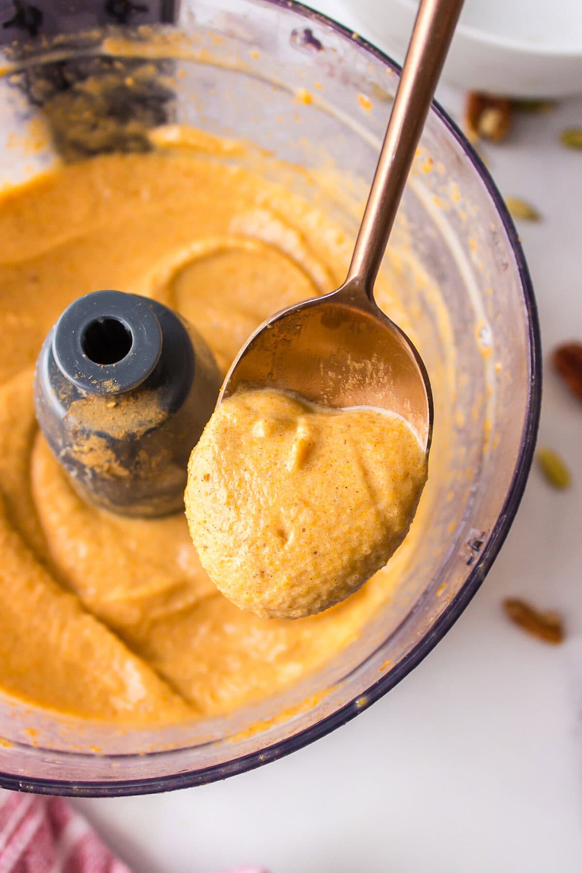 using a spoon to show the texture of the pumpkin smoothie in a blender. 