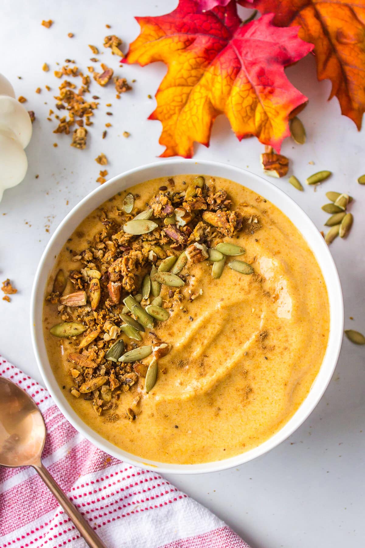 white bowl with pumpkin smoothie and toped with pumpkin seeds and granola. 