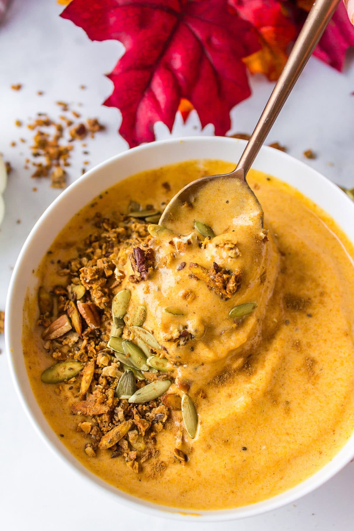 finished pumpkin smoothie in a white bowl with granola and pumpkin seeds on top.