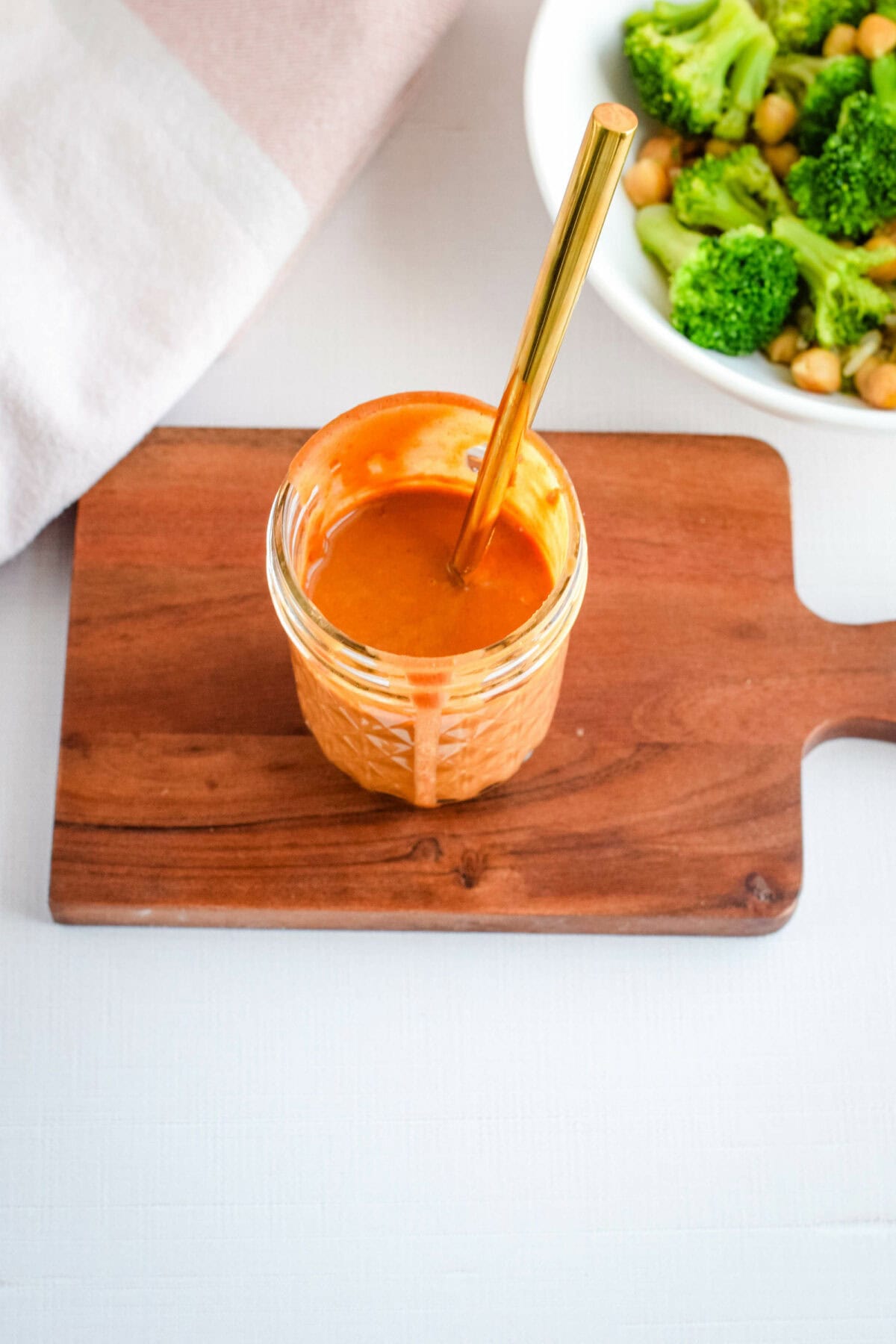 small mason jar filled with the Thai peanut sauce, sitting on a wooden board, and with a gold spoon inside.