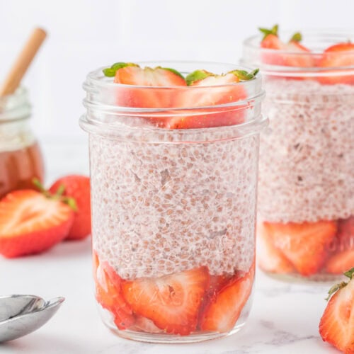 two mason jars filled with strawberries and plant based chia seed pudding layered in a mason jar like a parfait.